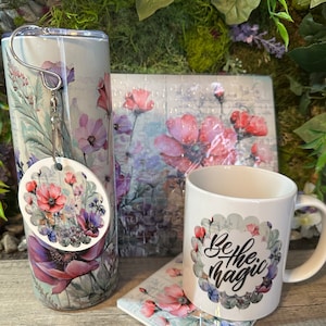 May include: A set of floral themed gifts including a white ceramic mug with the text "Be the magic" in black, a white tumbler with a floral design, a floral coaster, and a floral puzzle.