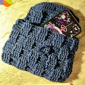 May include: A dark blue crocheted bag with a phone inside. The phone screen shows a black background with a clock, flowers, and butterflies.