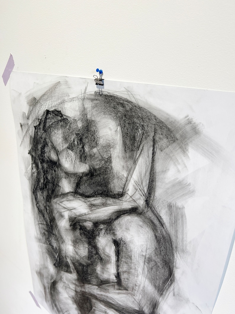 Op de afbeelding: Een zwart-witte houtskooltekening van twee figuren die elkaar omarmen. De tekening is gemaakt op een witte papieren achtergrond.