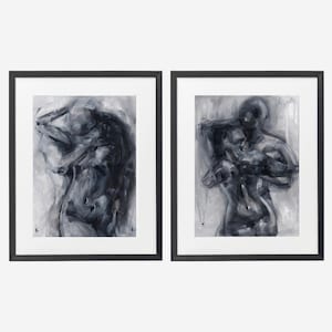 Op de afbeelding: Een set van twee ingelijste wandkunstwerken met abstracte, houtskoolkleurige schilderijen van menselijke figuren in een omhelzing. Elk stuk is gevat in een dunne zwarte lijst met een witte passe-partout, met expressieve penseelstreken.