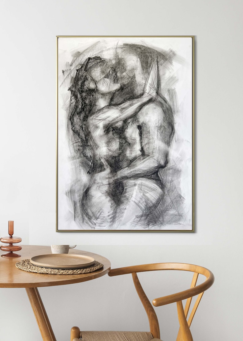 Op de afbeelding: Een zwart-witte houtskooltekening van een stel dat elkaar omhelst en kust. De tekening is ingelijst in een gouden lijst en hangt aan een witte muur.