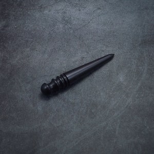 May include: A black wooden tool with a pointed end and a rounded handle. The tool is used for leather crafting.