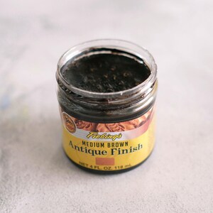 May include: A small glass jar of Fiebing's Medium Brown Antique Finish leather dye. The jar is filled with a dark brown liquid and has a yellow label with the product name and size: 4 fl oz (118 ml).