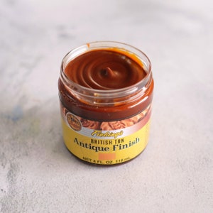 May include: A glass jar of Fiebing's British Tan Antique Finish leather dye. The jar is filled with a dark brown liquid and has a yellow label with the product name and size: "NET 4 FL. OZ. 118 ml".