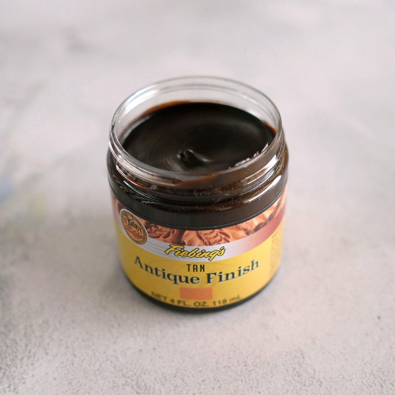 May include: A small jar of Fiebing's Tan Antique Finish leather dye. The jar is open and the dye is a dark brown color. The jar is labeled with the Fiebing's logo and the words "Tan Antique Finish".