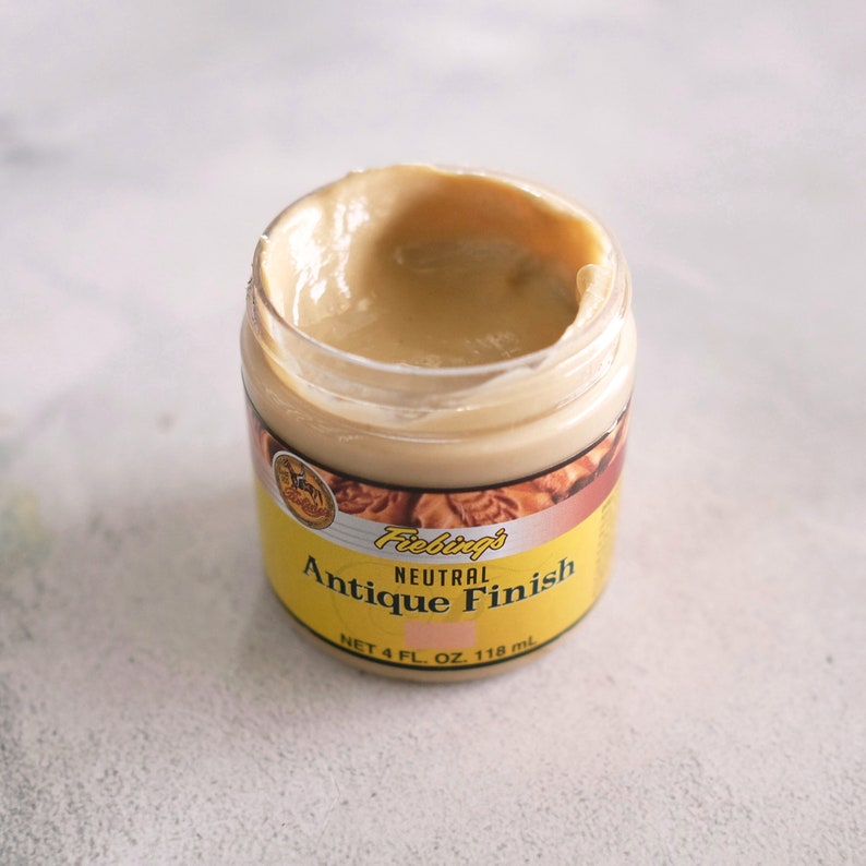 May include: A jar of Fiebing's Neutral Antique Finish, a leather treatment product. The jar is open and the product is a light brown color. The jar is labeled with the product name and size: "NET 4 FL. OZ. 118 ml".