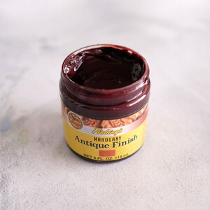 May include: A small jar of Fiebing's Mahogany Antique Finish leather dye. The jar is yellow with black lettering and a brown label. The dye is a dark red color.