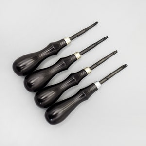 May include: Set of four black handled tools with silver accents. The tools have different sized blades and are used for leather crafting.