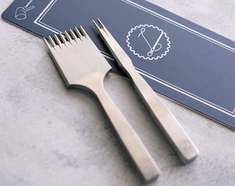 May include: Two silver leather crafting tools. One tool has a handle and a row of small, sharp points. The other tool has a handle and two sharp points. The tools are on a blue background with the text "LeatherCraft" and a logo.
