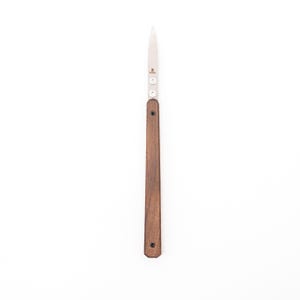 May include: A small, stainless steel knife with a pointed blade and a dark brown wooden handle. The knife has a simple design with a few circular details near the blade's base. The handle is rectangular and secured with small rivets.