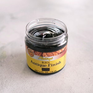 May include: A clear jar with a black liquid inside. The label reads "Fiebing's Black Antique Finish" and "Net 4 fl. oz. 118 ml".