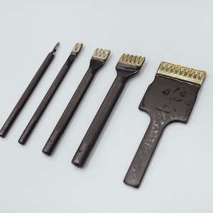 May include: A set of five leather working tools. The tools are dark metal with textured handles and various shaped heads, including a pointed awl, a single-prong tool, and multi-prong tools. The largest tool has the number "2" stamped on it.
