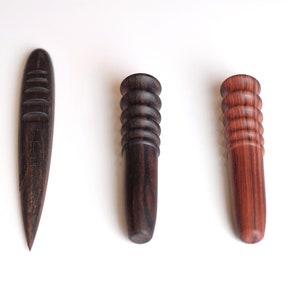 May include: Three wooden tools for leather crafting. The tool on the left is a pointed awl with a grooved handle. The two tools on the right are rounded and have a grooved handle.