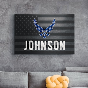 May include: A grey sofa with a yellow cushion in front of a canvas print featuring a blue Air Force logo and the name "JOHNSON" printed in white.