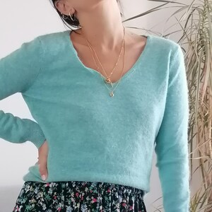 May include: A turquoise blue v-neck sweater with long sleeves and a floral print skirt.