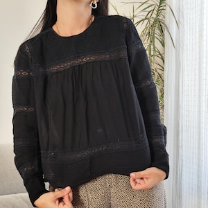 May include: Black long-sleeve top with lace detailing and a round neckline. The top has a textured bodice and sleeves. The model is wearing tan and black spotted pants. The outfit is suitable for casual wear.