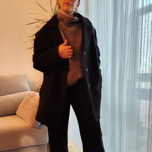 May include: A woman wearing a black coat, black pants, and a gray sweater. She is wearing silver earrings and silver sneakers.