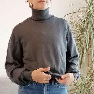 Puede incluir: Un jersey gris de cuello alto con mangas largas. El jersey está hecho de un material suave y cómodo y es perfecto para superponer.