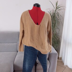 Peut inclure: Un pull en tricot beige avec un col en V profond et des manches longues, associé à un jean bleu.