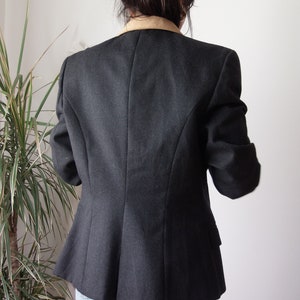 以下が含まれることがあります： 茶色の襟が付いた濃いグレーのブレザー。ブレザーは体にフィットしたシルエットで、長袖です。