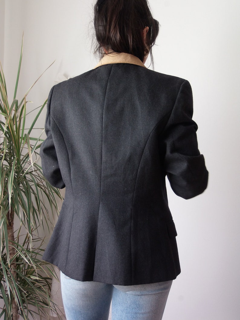 以下が含まれることがあります： 茶色の襟が付いた濃いグレーのブレザー。ブレザーは体にフィットしたシルエットで、長袖です。