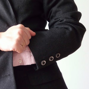 以下が含まれることがあります： ピンクと白のストライプのシャツを着た黒のブレザー。ブレザーの袖にはボタンが4つ付いています。