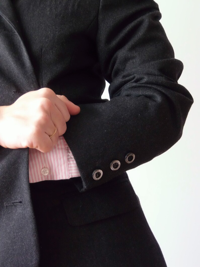 以下が含まれることがあります： ピンクと白のストライプのシャツを着た黒のブレザー。ブレザーの袖にはボタンが4つ付いています。