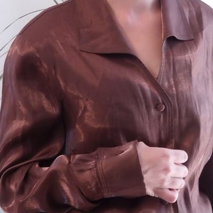 May include: A brown satin blouse with a button-up front and long sleeves.