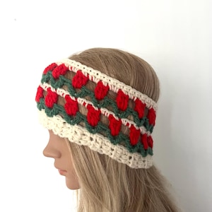 May include: A white crocheted headband with a red and green pattern. The headband has a repeating pattern of red hearts with green leaves.