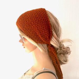May include: A rust-coloured knitted headband tied in a knot at the back of the head.