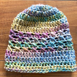 May include: A colorful crocheted beanie hat with a multi-colored yarn in shades of blue, green, yellow, and purple.