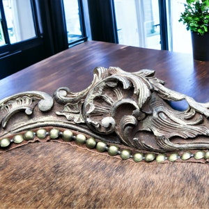 Pu&ograve; includere: Primo piano di una sedia in pelle marrone con dettagli decorativi dorati e una fila di chiodi dorati lungo il bordo.