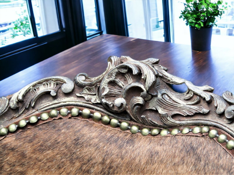 Pu&ograve; includere: Primo piano di una sedia in pelle marrone con dettagli decorativi dorati e una fila di chiodi dorati lungo il bordo.