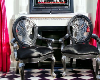 May include: Two black chairs with silver accents and black cowhide upholstery. The chairs have ornate carved backs and scrolled legs. The chairs are in front of a fireplace with a white mantel.