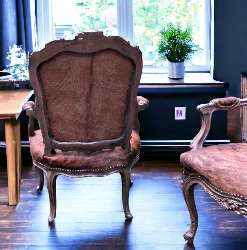 Pu&ograve; includere: Due sedie antiche con rivestimento in pelle marrone e cornici in legno ornate. Le sedie sono posizionate in una stanza con una finestra e un pavimento in legno.