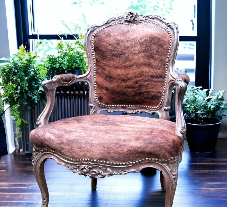 Pu&ograve; includere: Una poltrona in stile vintage con rivestimento in pelle di mucca marrone e bianca. La sedia ha una struttura in legno intagliato con dettagli decorativi e una finitura argentata.