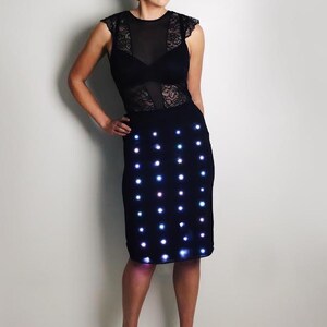 Pode incluir: Vestido preto com corpete de renda e saia adornada com filas de luzes LED brancas. O vestido é usado com saltos pretos. O design é moderno e elegante, perfeito para um evento especial.