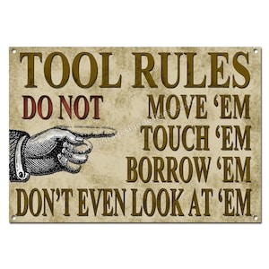 May include: A vintage-style sign with a brown background and gold text that reads "TOOL RULES DO NOT MOVE 'EM TOUCH 'EM BORROW 'EM DON'T EVEN LOOK AT 'EM". A hand pointing to the right is shown in the upper left corner of the sign.