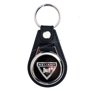 Puede incluir: Llavero de cuero negro con un círculo de metal plateado que presenta el logotipo de Reliant. El logotipo es un triángulo plateado con un castillo en su interior y la palabra "Reliant" encima.