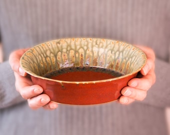 May include: A person is holding a brown ceramic bowl with a green and brown glaze. The bowl is empty.