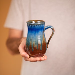 May include: A blue and brown ceramic mug with a handle. The mug has a glaze that creates a drip effect.