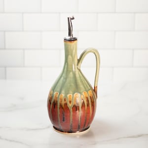 May include: A ceramic olive oil bottle with a green and brown glaze. The bottle has a spout and a handle.