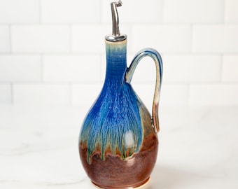 May include: A blue and brown ceramic oil and vinegar bottle with a silver pour spout and a handle.