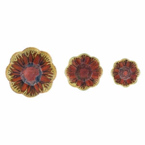 May include: Three decorative flower-shaped dishes. The dishes have a red center with a gold-colored rim and petal-like edges. The sizes vary, with the largest dish on the left and the smallest on the right.