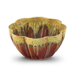 May include: A ceramic bowl with a unique, scalloped rim. The bowl features a rich, reddish-brown base with a textured, dripped glaze in shades of olive green and tan around the rim. The bowl's design is both functional and decorative.