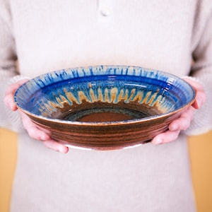 May include: A large, brown ceramic bowl with a blue and brown glaze. The bowl has a wide, shallow shape and a slightly flared rim.