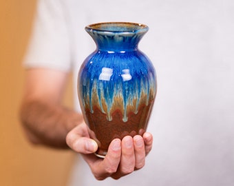 May include: A blue and brown ceramic vase with a drip glaze design. The vase is hand-crafted and has a unique, rustic look.