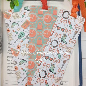 May include: Three decorative bookmarks with colorful patterns and ribbons. One bookmark features musical instruments and the text "HOW GIRL". Another has records and locks. The third bookmark has bows, lipstick, and the text "SHOW GIRL".