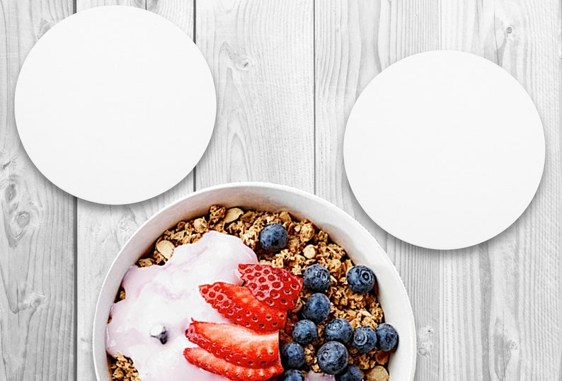 May include: A white bowl filled with granola, yogurt, blueberries, and strawberries. The bowl is on a white wooden surface.