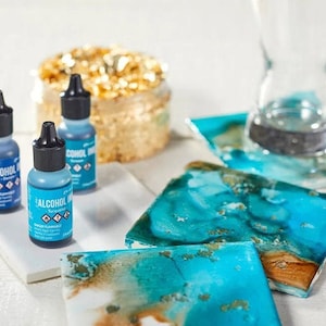 May include: Three bottles of alcohol ink in turquoise, teal, and denim blue. The bottles are labeled "Alcohol Ink" and have a dropper top. The ink is used for creating art on various surfaces, such as resin, epoxy, and alcohol inks.